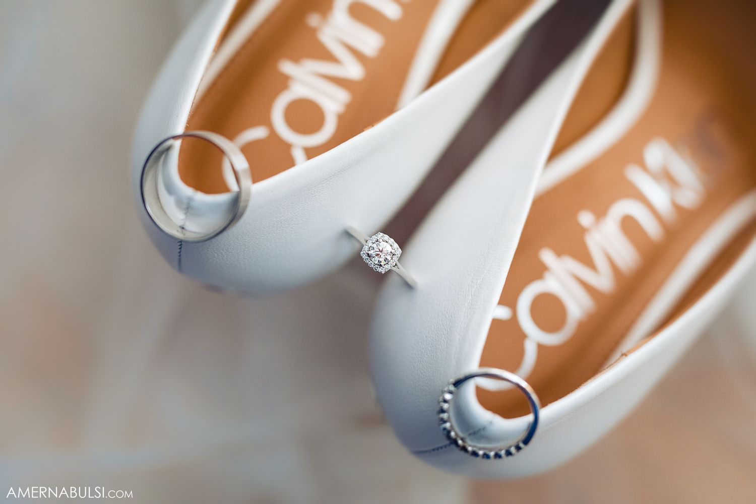 Wedding rings and bridal shoes arranged on a beige surface with soft lighting creating elegant shadows.
