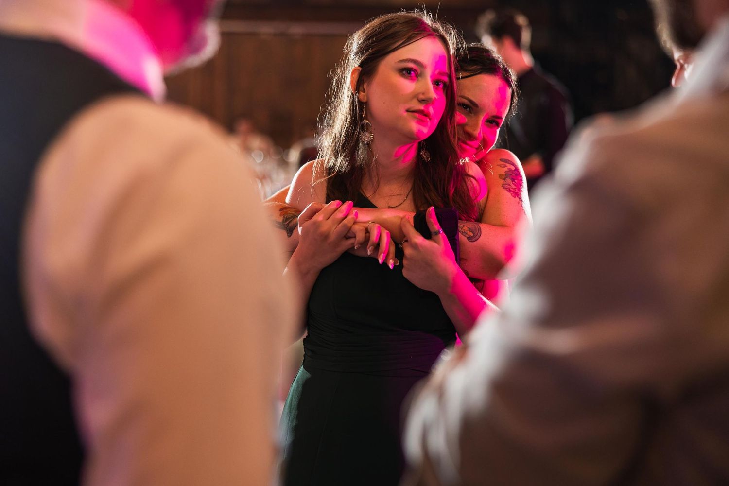 Guests dance together under pink and purple lighting at an evening wedding reception.