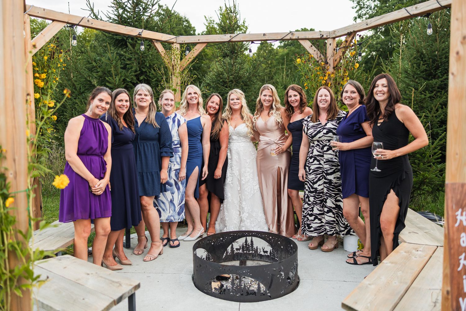 A gathering of people in cocktail dresses stand together on a patio beneath a wooden pergola structure.