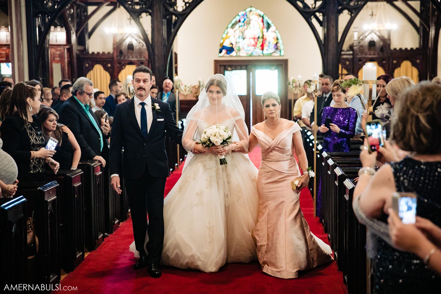 Wedding ceremony guests and wedding party inside a church with elegant architectural details.