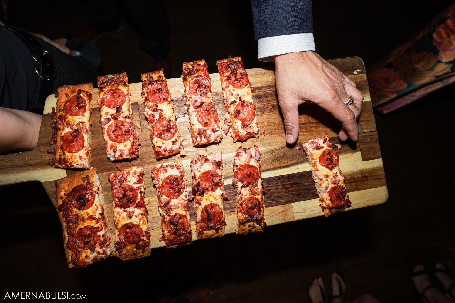 A wooden serving board with sliced pepperoni pizza squares being served at a party.