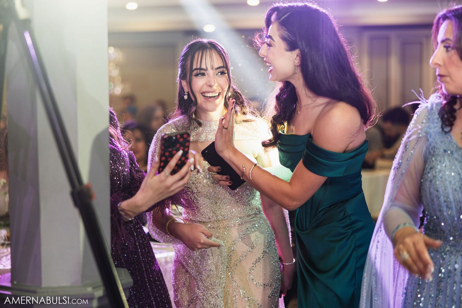 Wedding reception guests dancing and celebrating in elegant evening attire under purple lighting.