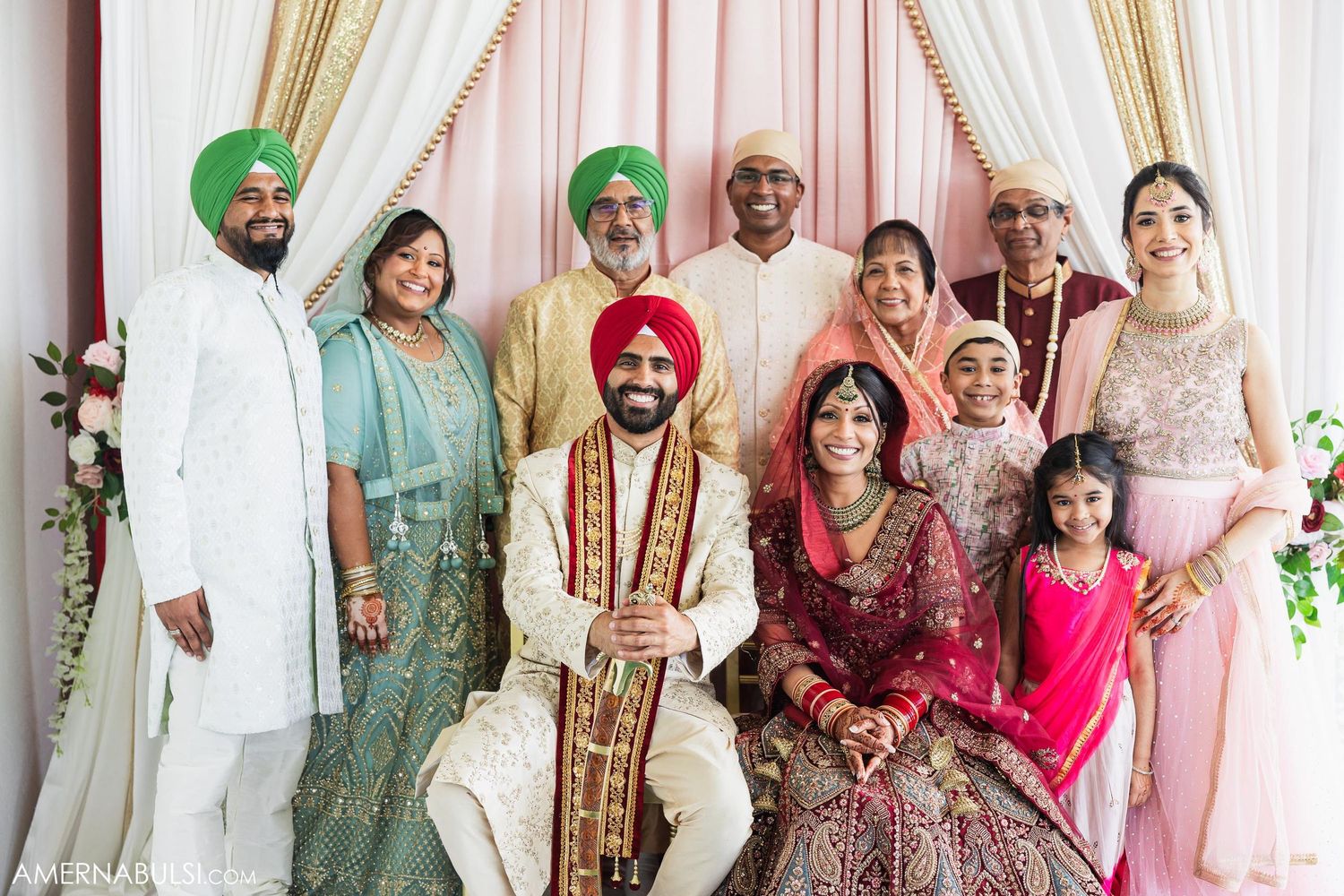 Traditional Sikh wedding family portrait with decorative backdrop and cultural attire.
