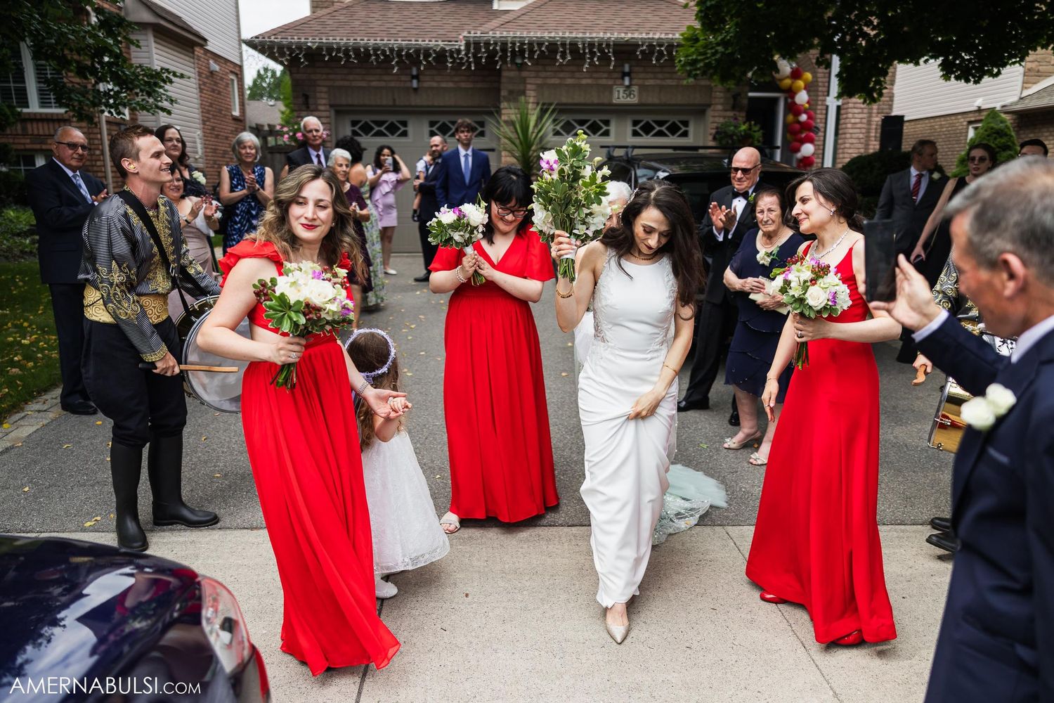 Wedding party in red dresses and formal attire walking outside during celebration.