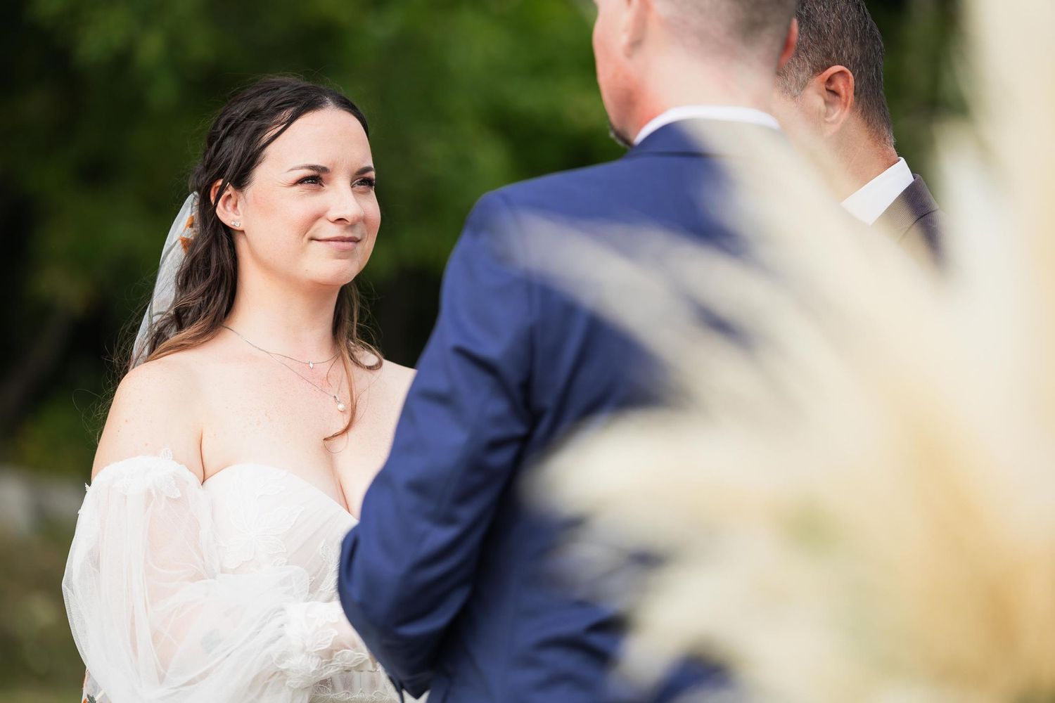 A tender wedding moment captured outdoors with soft lighting and pampas grass in the foreground.