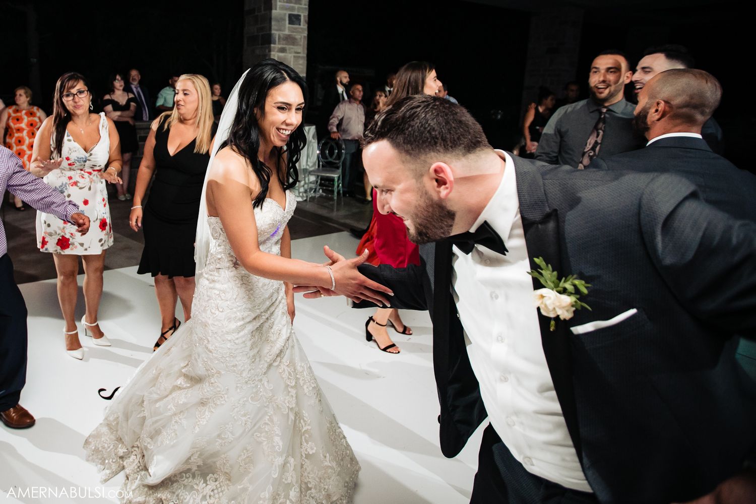 Newlyweds dancing energetically on white dance floor during wedding reception.