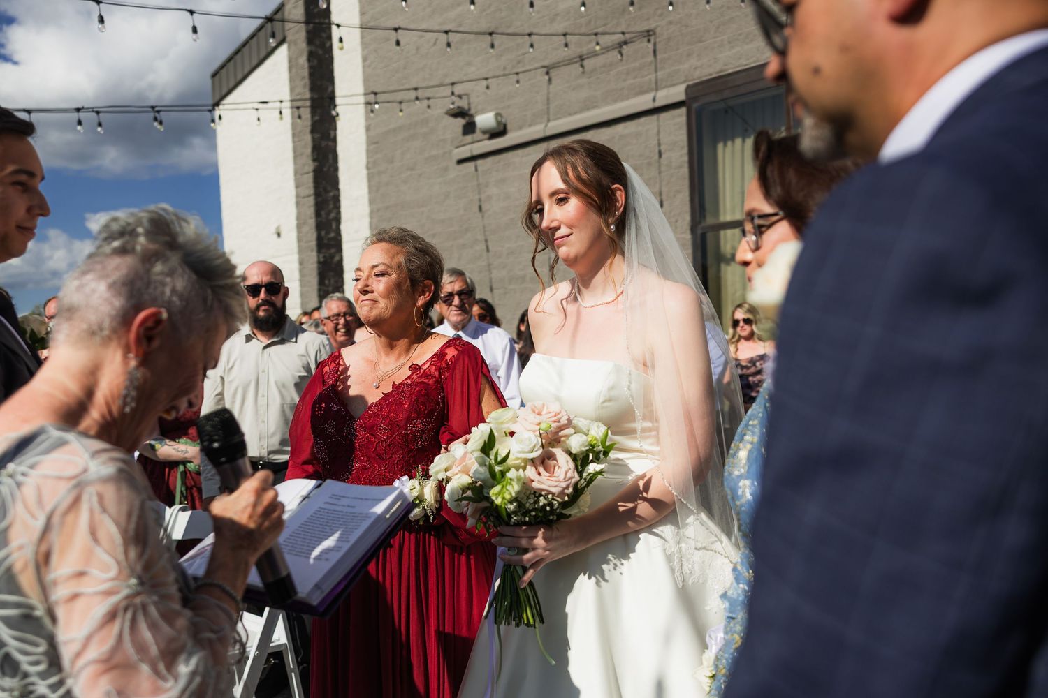Bride in white gown holding bouquet at outdoor ceremony.