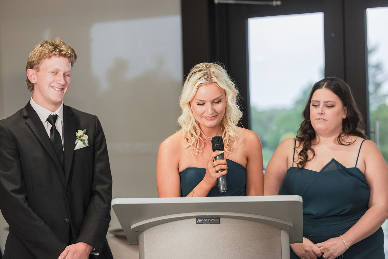 Bridesmaid delivers a heartfelt speech at a podium flanked by two attendants at a wedding reception.