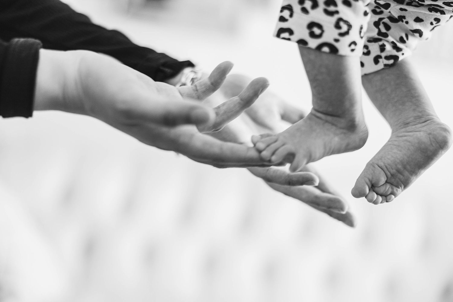 Black and white close-up of hands reaching toward each other against a light background.