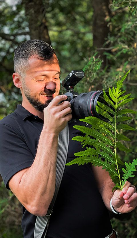 Professional photographer shooting through foliage in outdoor natural setting.