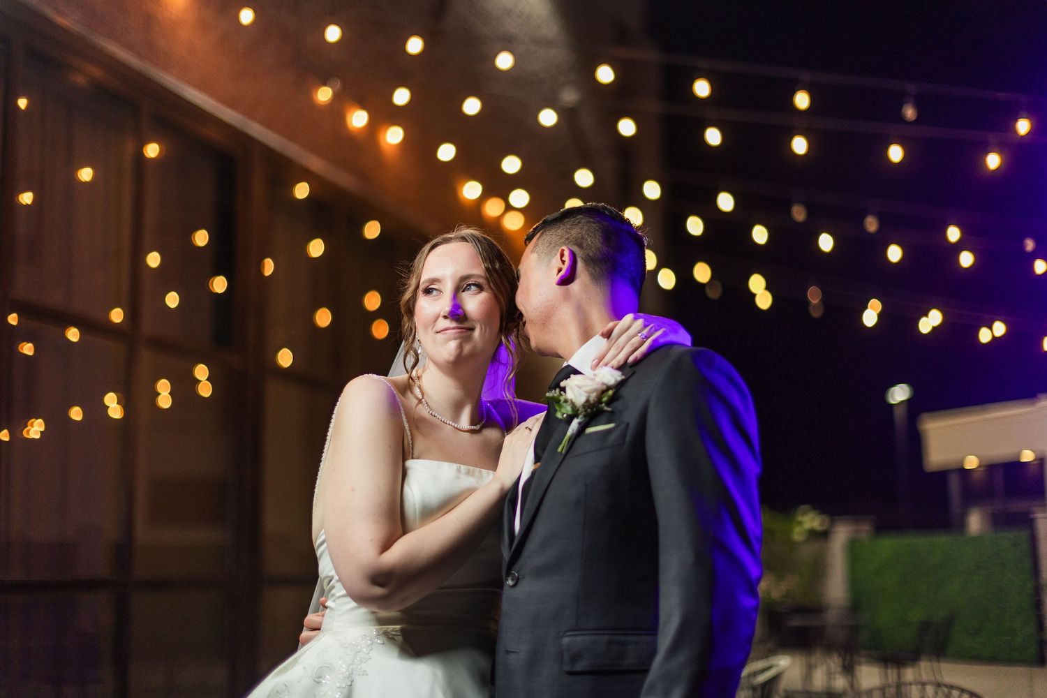 Bride and groom share romantic first dance under warm string lights at elegant outdoor evening wedding reception.