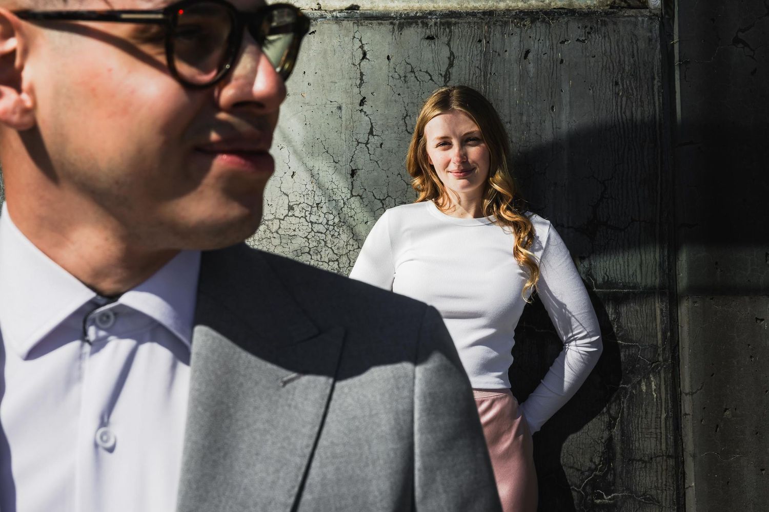 Artistic urban engagement photo with couple against industrial wall.