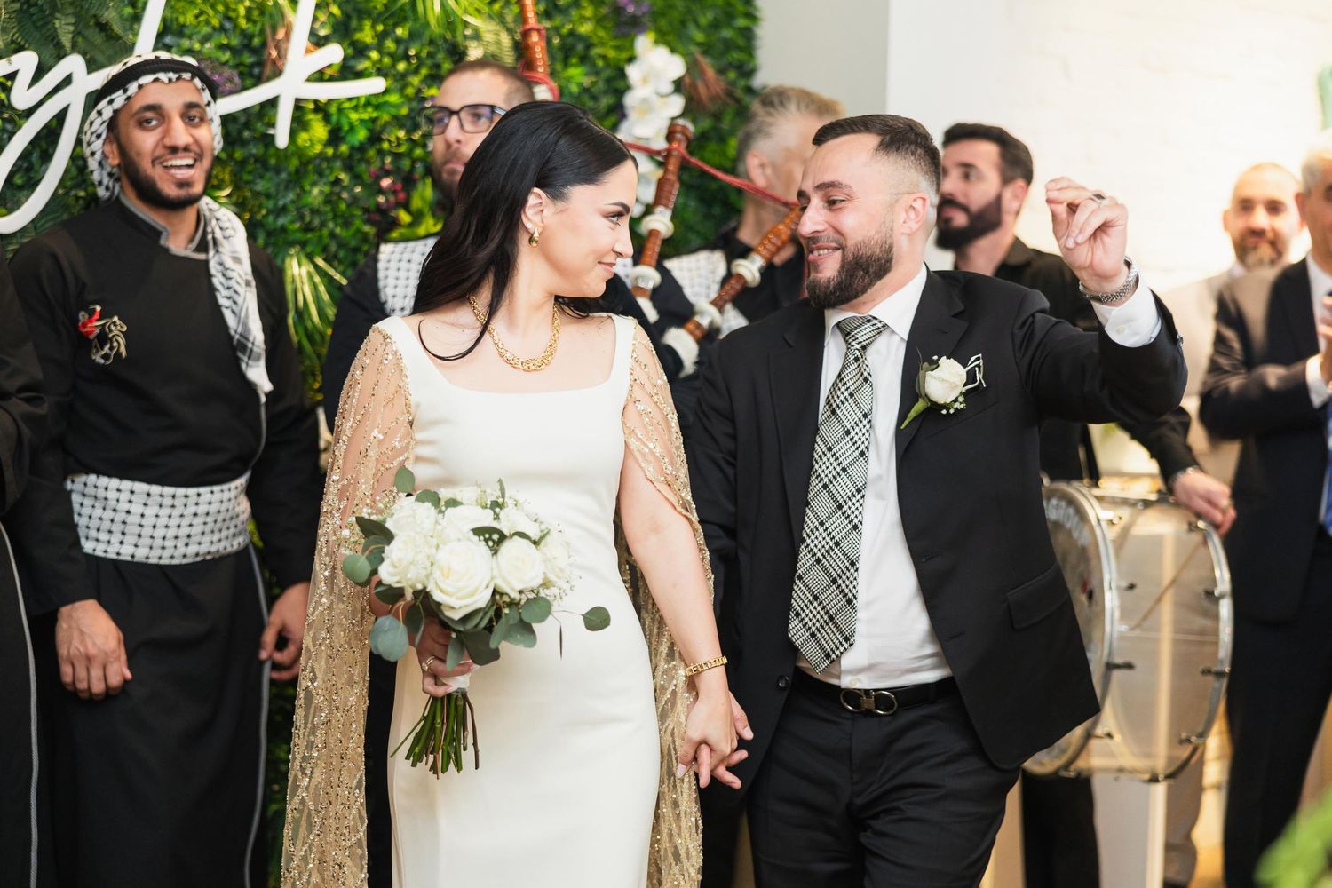 Couple walking through their wedding celebration while guests cheer in a modern venue.