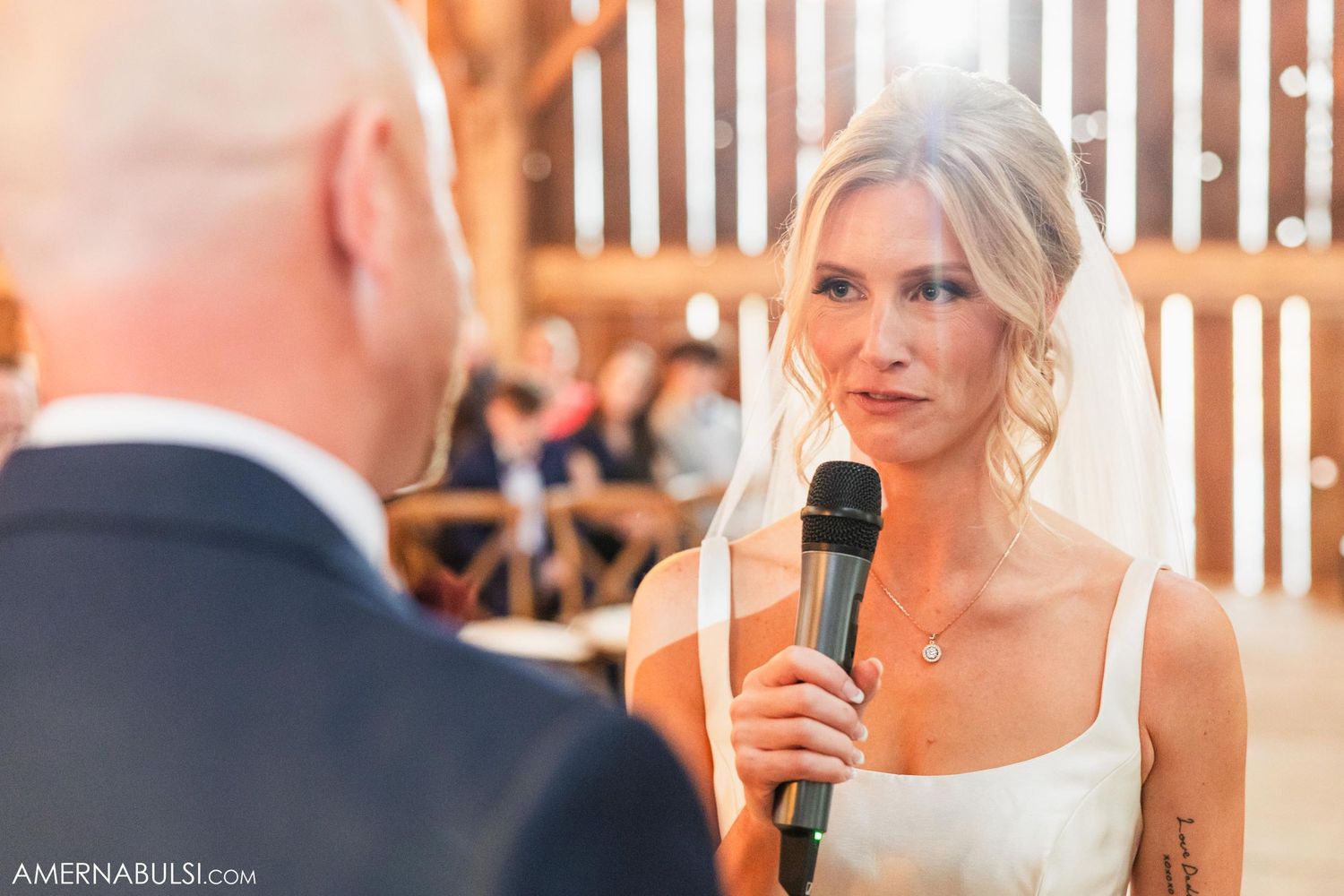Bride speaking vows into microphone during rustic barn wedding ceremony.