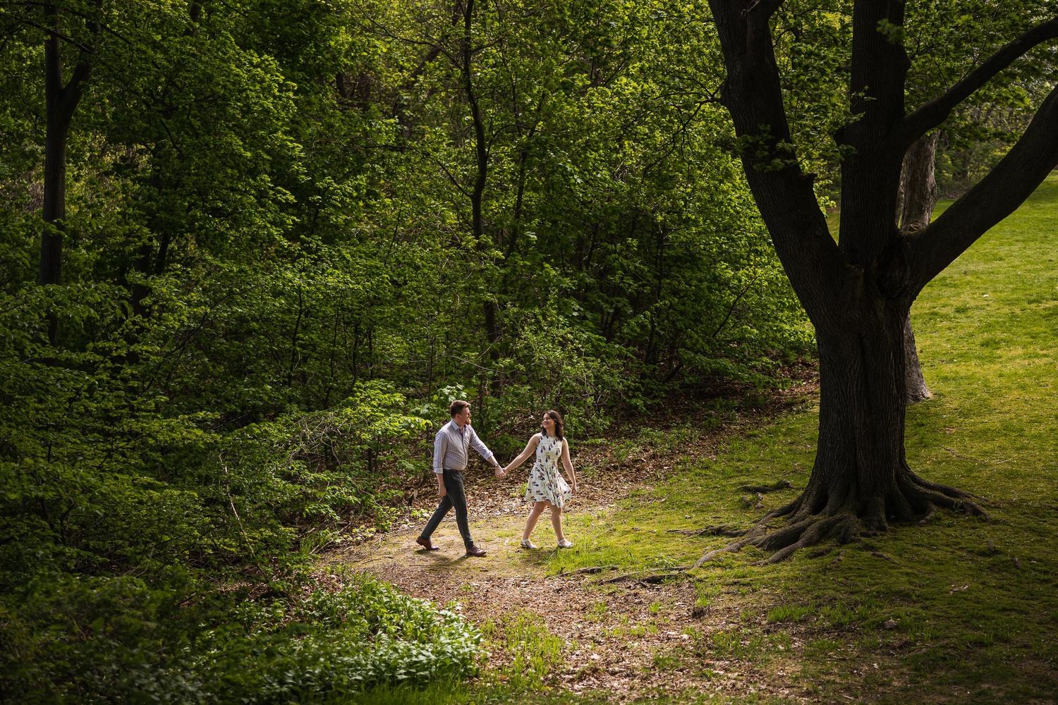 Couple walking hand in hand along forest path in dappled sunlight.