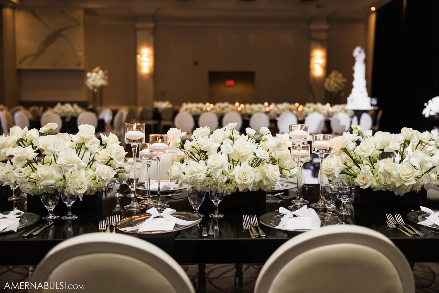 Wedding reception tables decorated with white floral centerpieces and black linens in a ballroom setting.