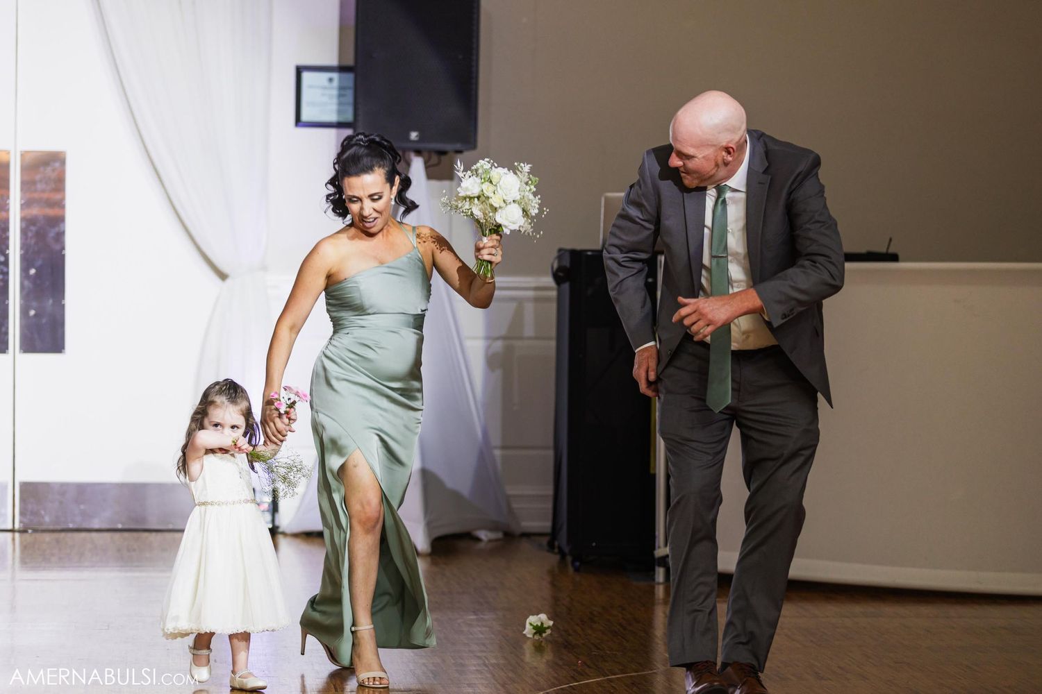 Wedding party members make a joyful entrance during reception while holding flowers and smiling.