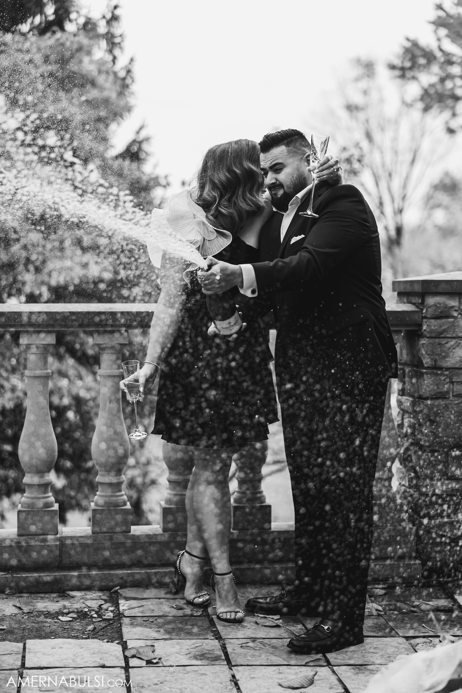 A couple celebrating with champagne spray on a stone terrace.