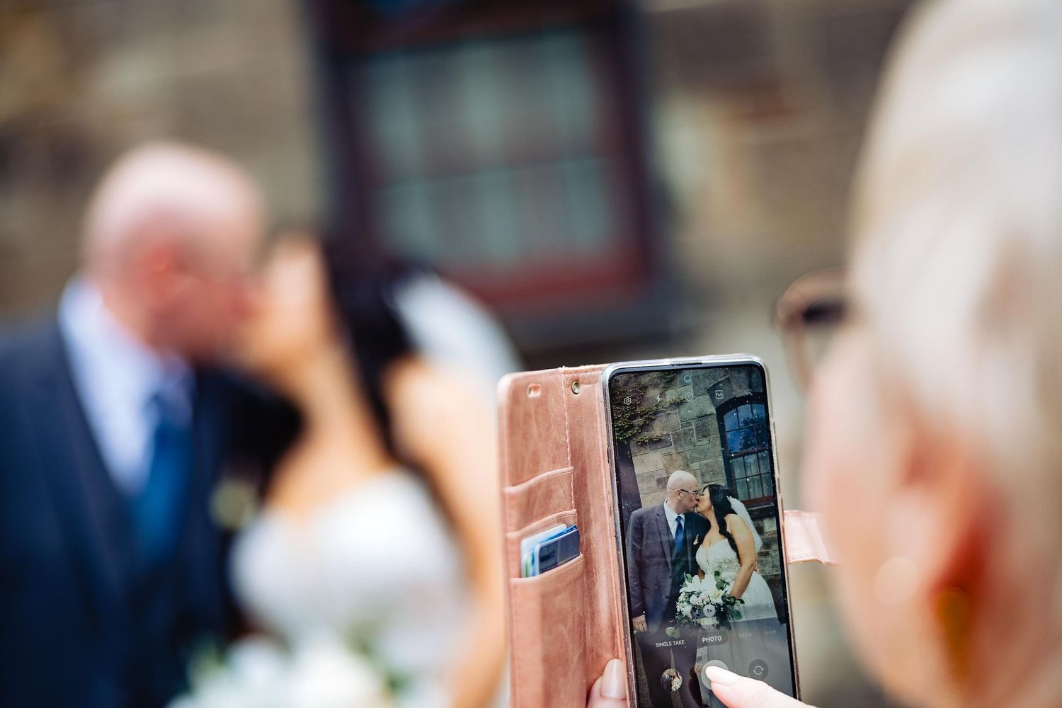 Someone capturing a wedding moment on a smartphone with blurred background.