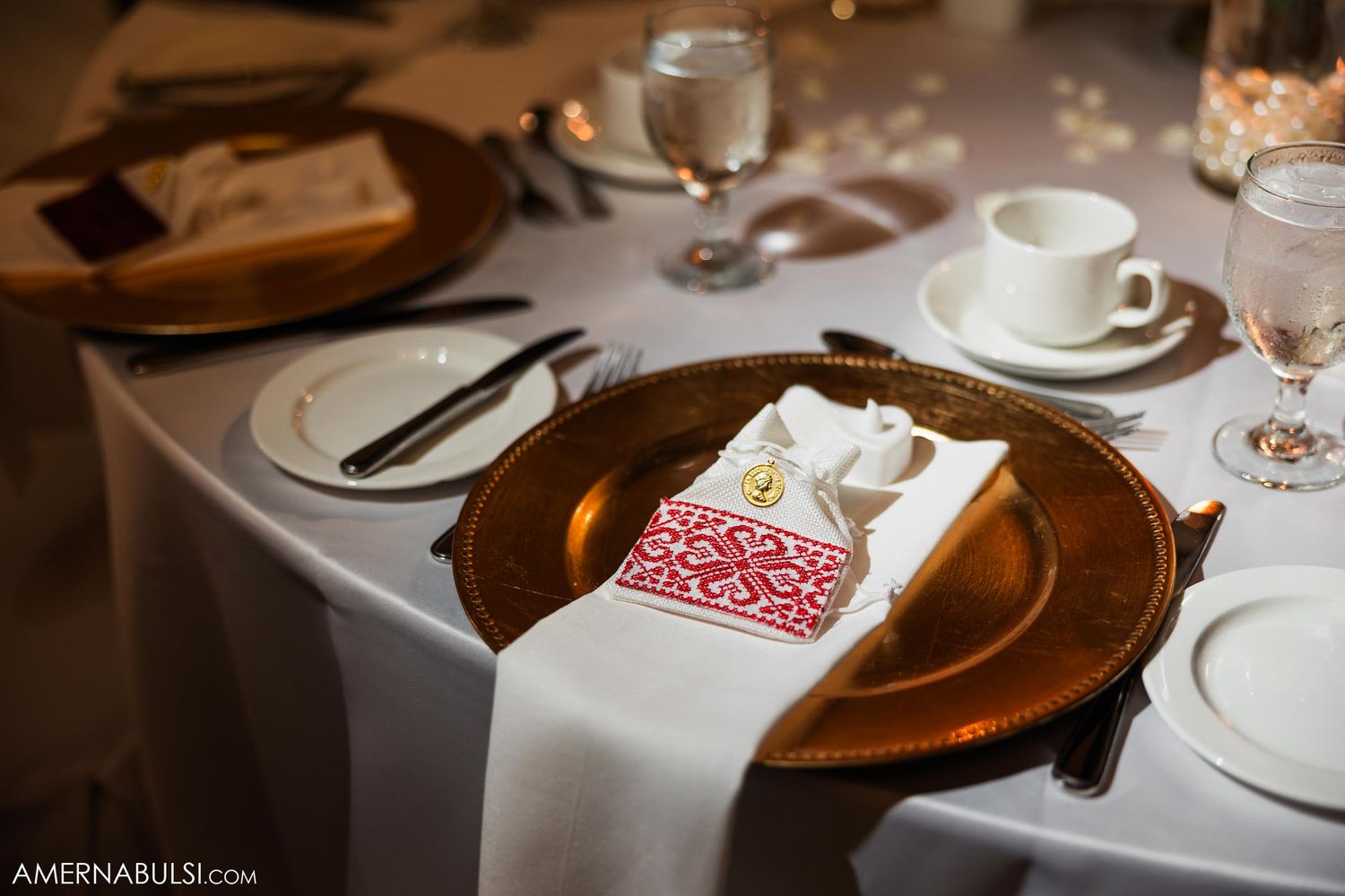 Formal table setting with gold charger plates and red napkin accents at wedding reception.