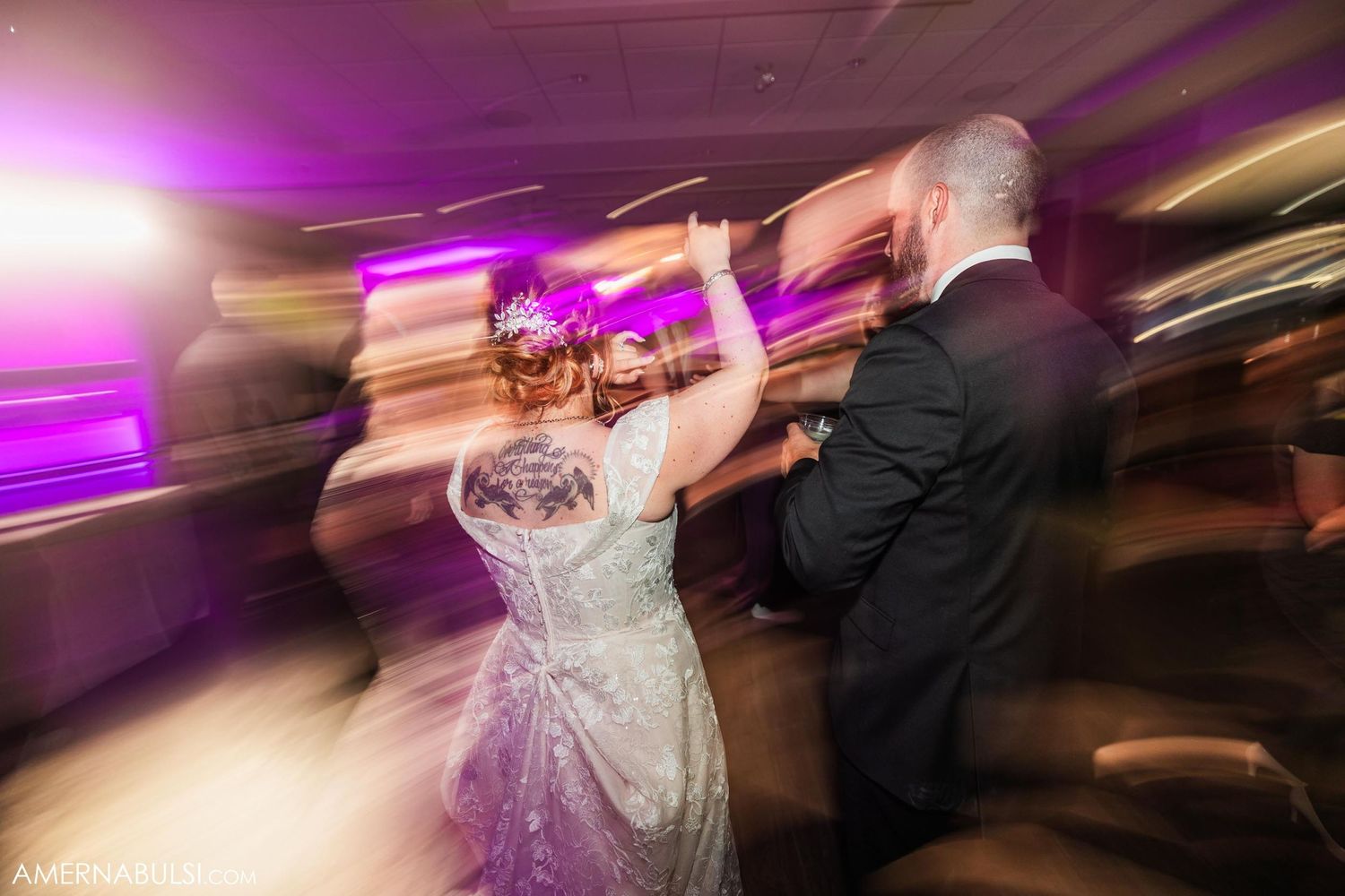 Motion-blurred photo of dancing couple spinning on dance floor with purple ambient lighting.