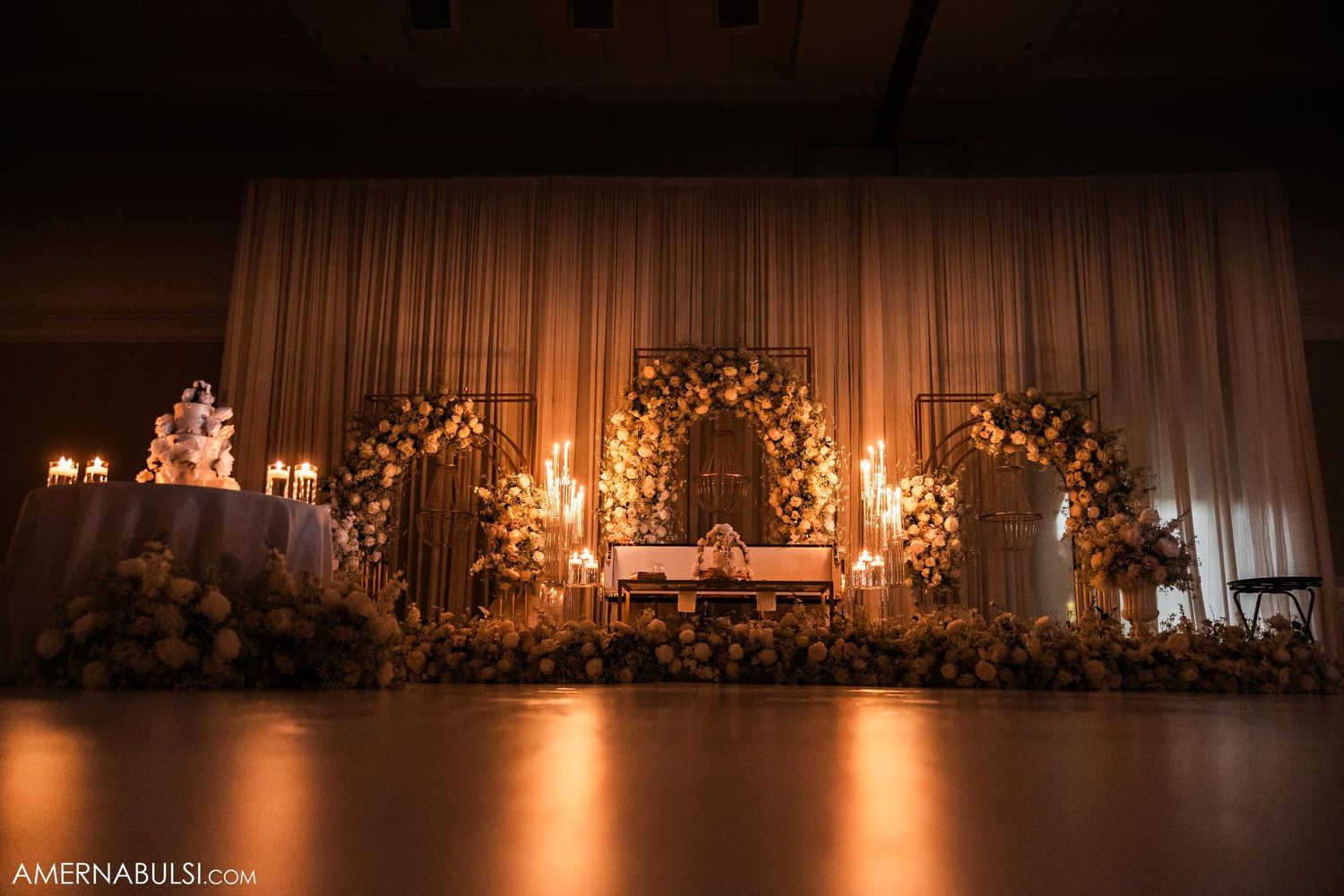 Romantic wedding stage setup with floral arch and warm ambient lighting.