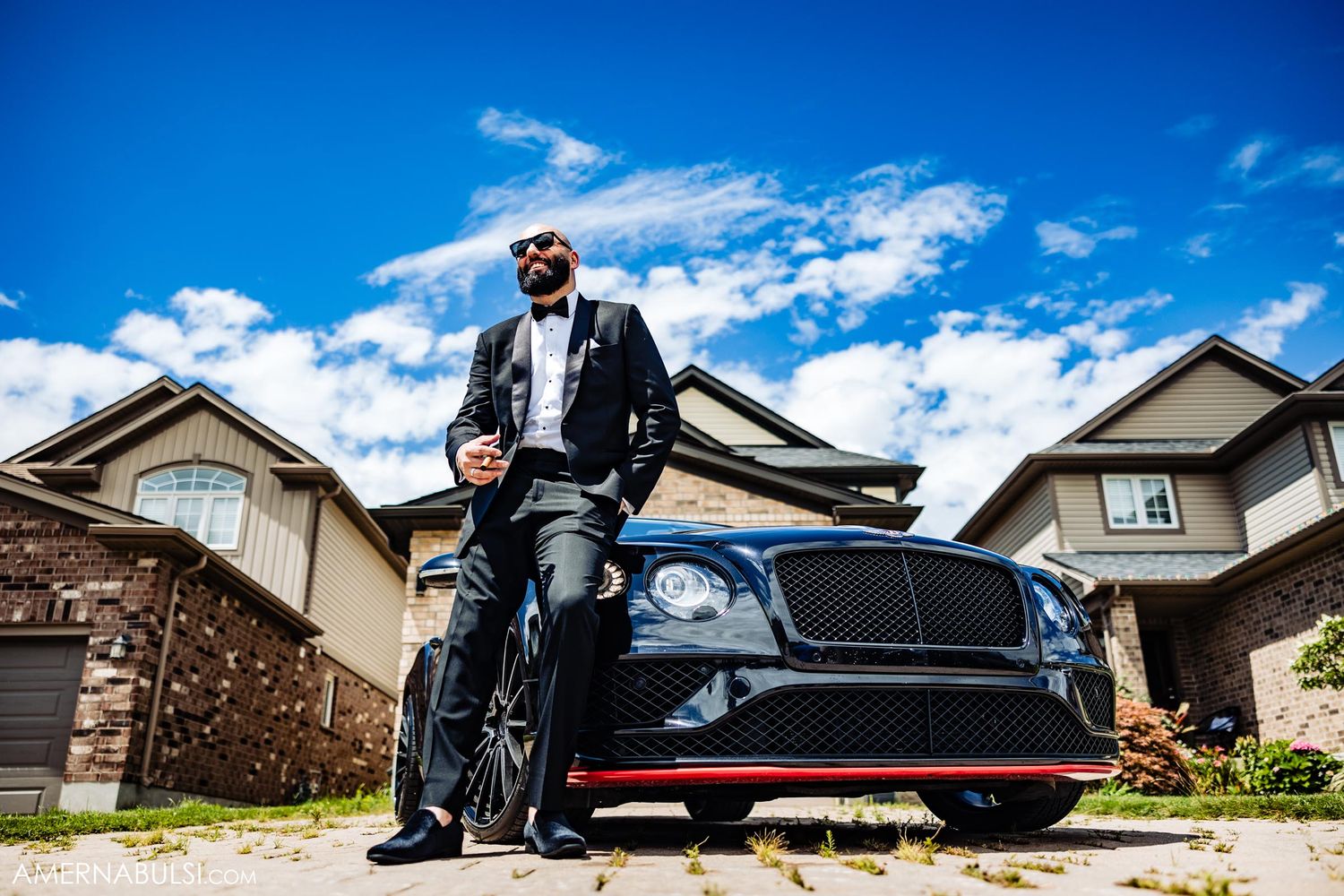 Father and son pose with black luxury car on suburban driveway.