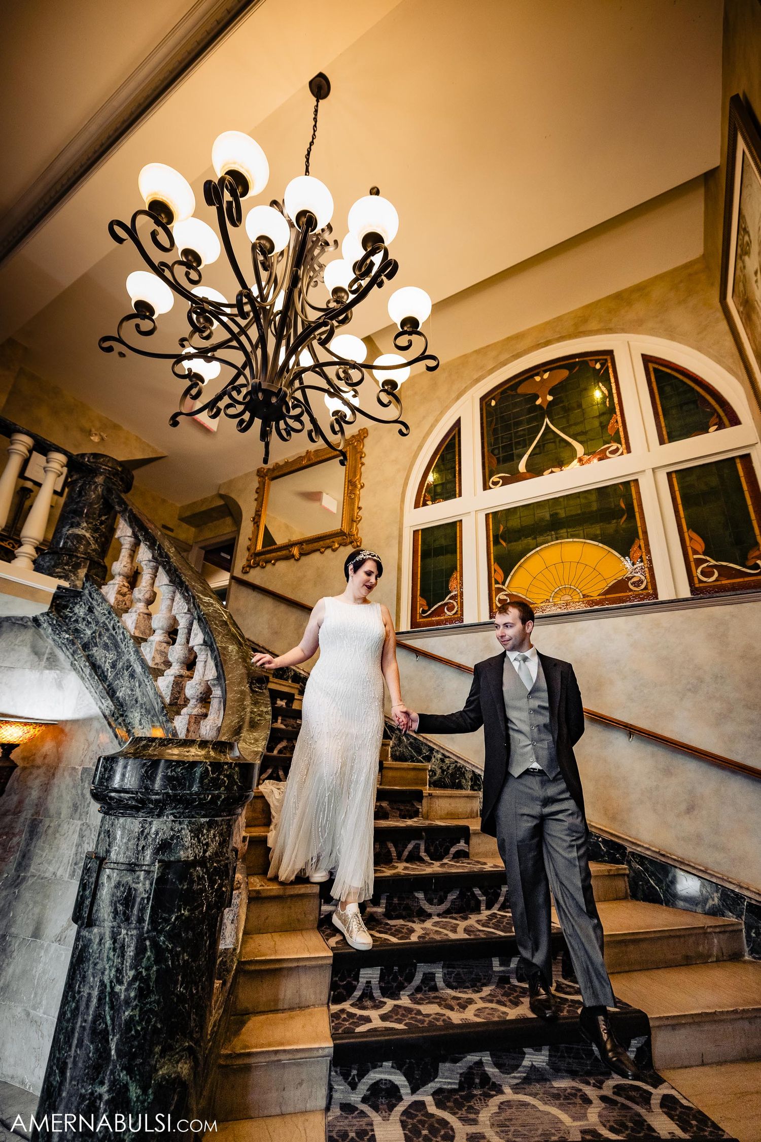 Elegant staircase photo with ornate chandelier and arched windows in vintage setting.