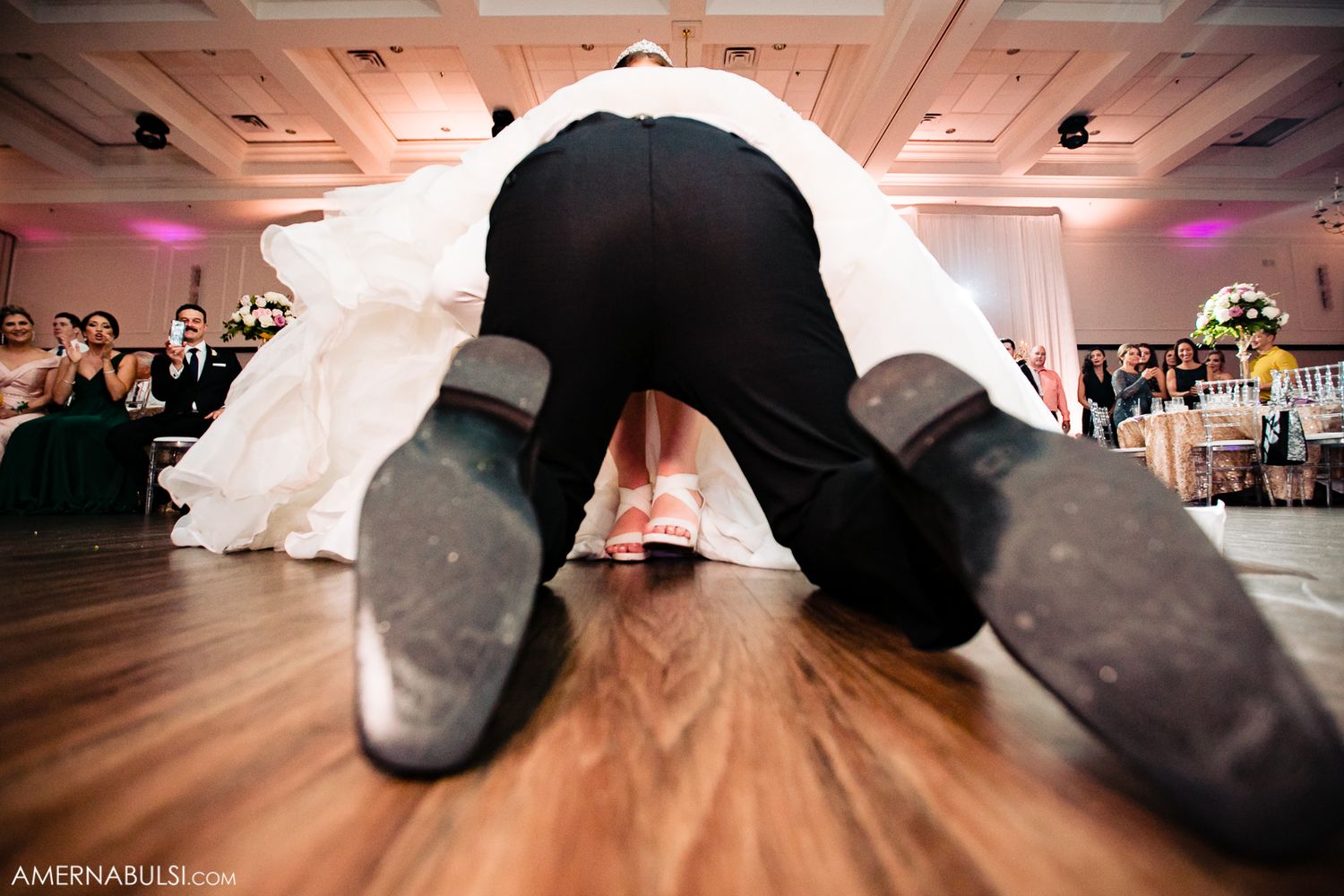 A close-up view of dancing feet at a wedding reception shows dress shoes and a white gown on the dance floor.