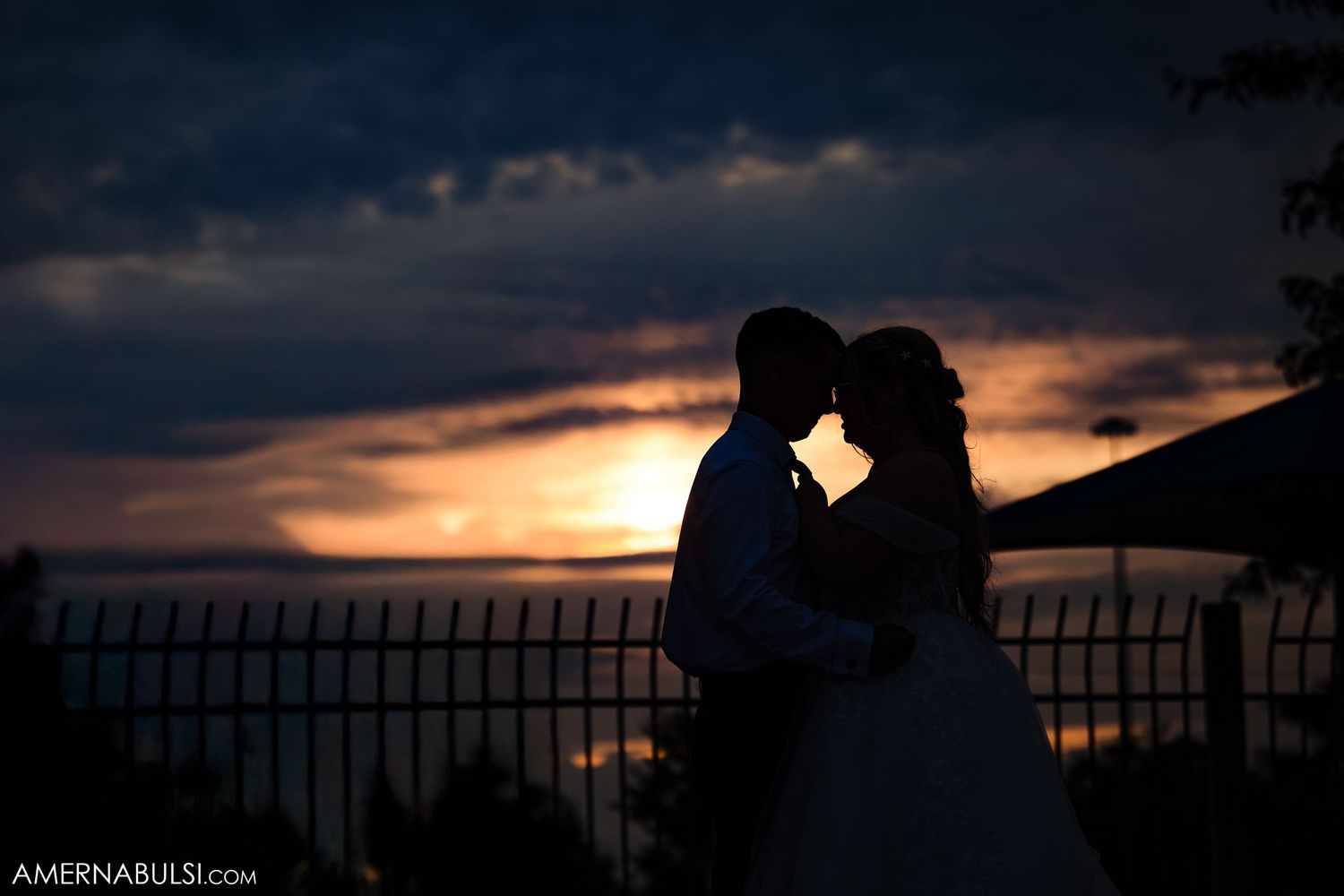 Dramatic silhouette shots of newlyweds against a sunset sky with ornate fence backdrop.