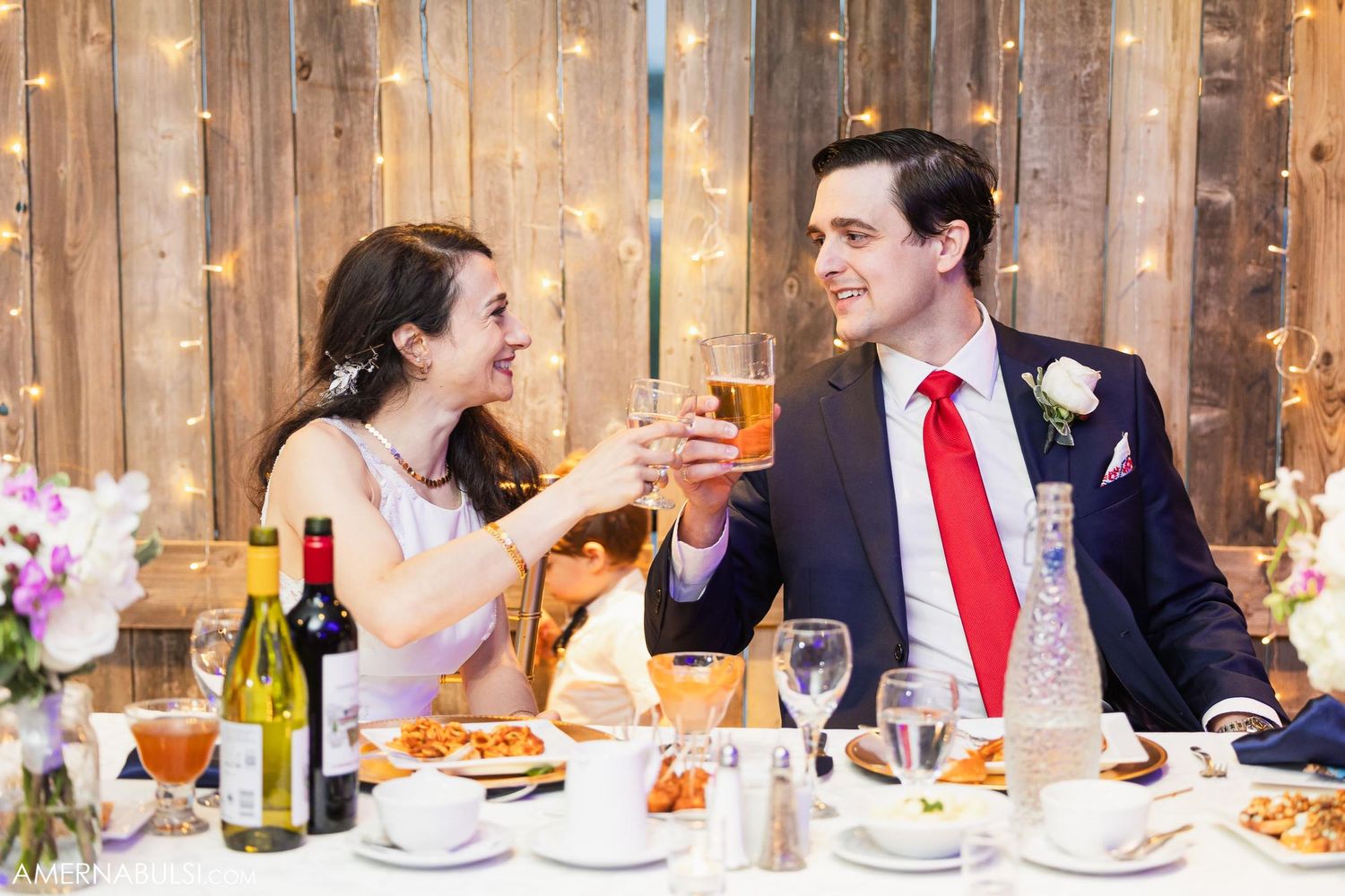 Couple toasting with cocktails at their wedding reception dinner table.