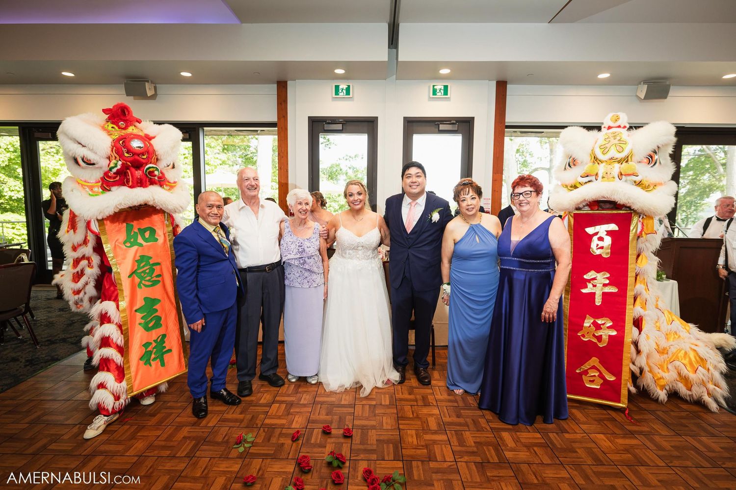 Wedding party poses with traditional Chinese lion dance performers at indoor celebration.