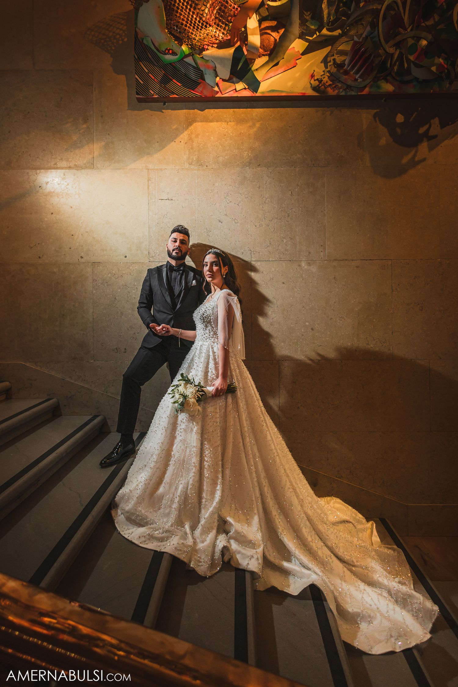 Dramatic wedding portrait on stairs with artistic lighting and flowing bridal gown train.