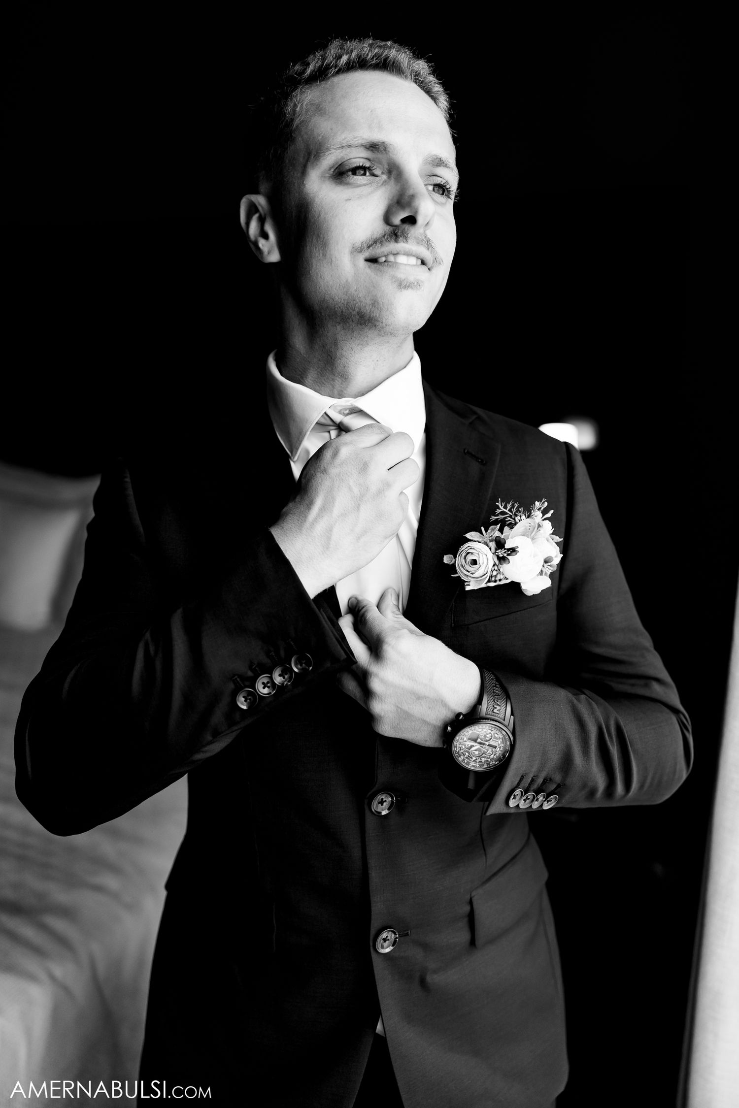 Dramatic black and white portraits of a groom adjusting his tie and boutonniere.