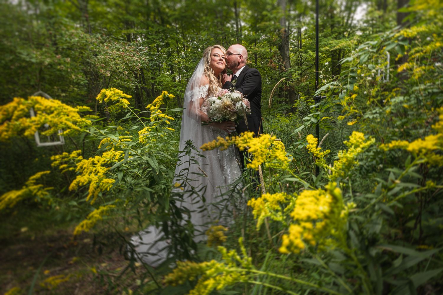 Wedding couple poses among vibrant yellow wildflowers in a serene woodland setting.