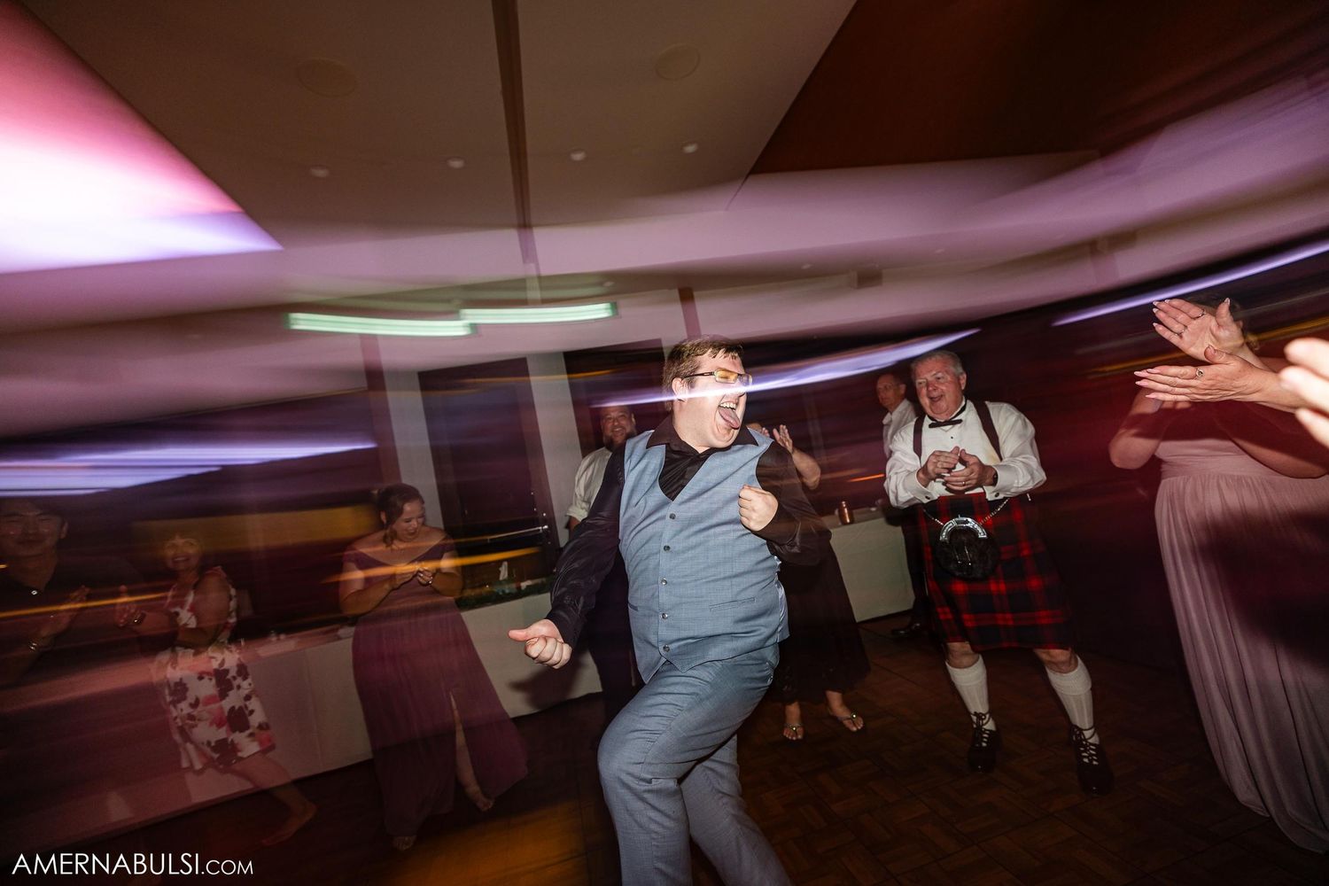 Wedding guest dancing enthusiastically under pink ambient lighting at reception.