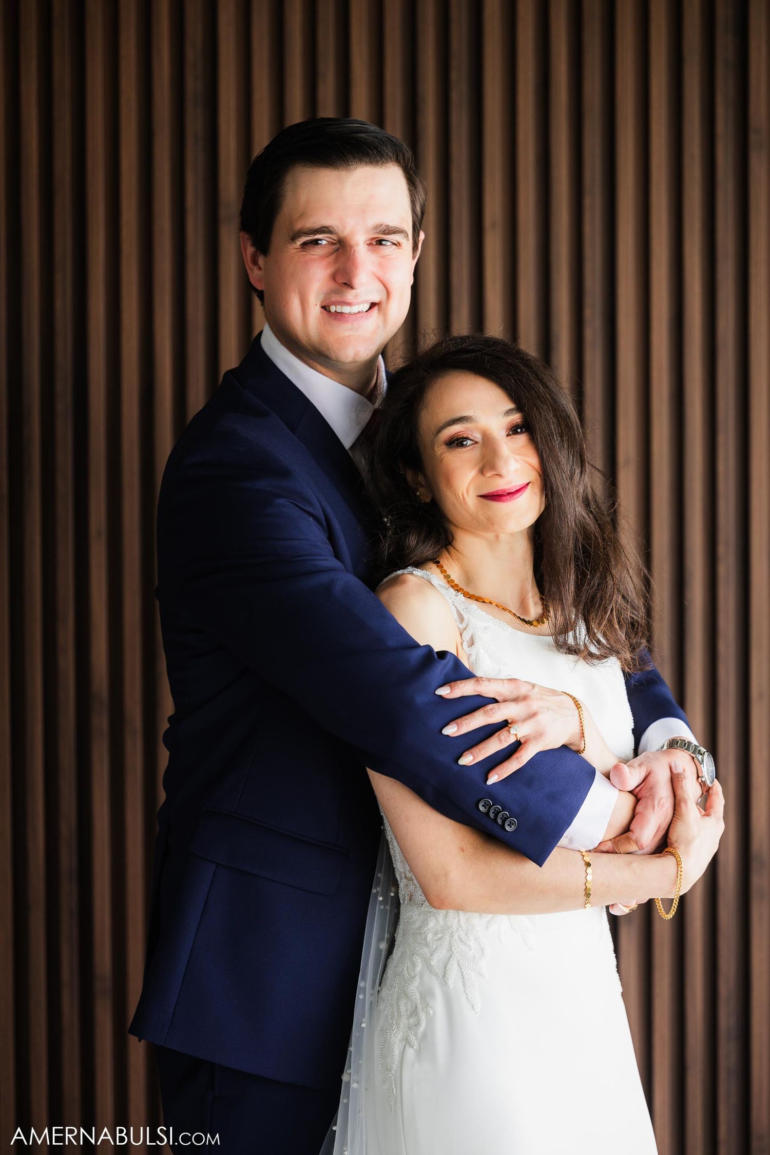 A romantic portrait of a newlywed couple against a striped wall background.
