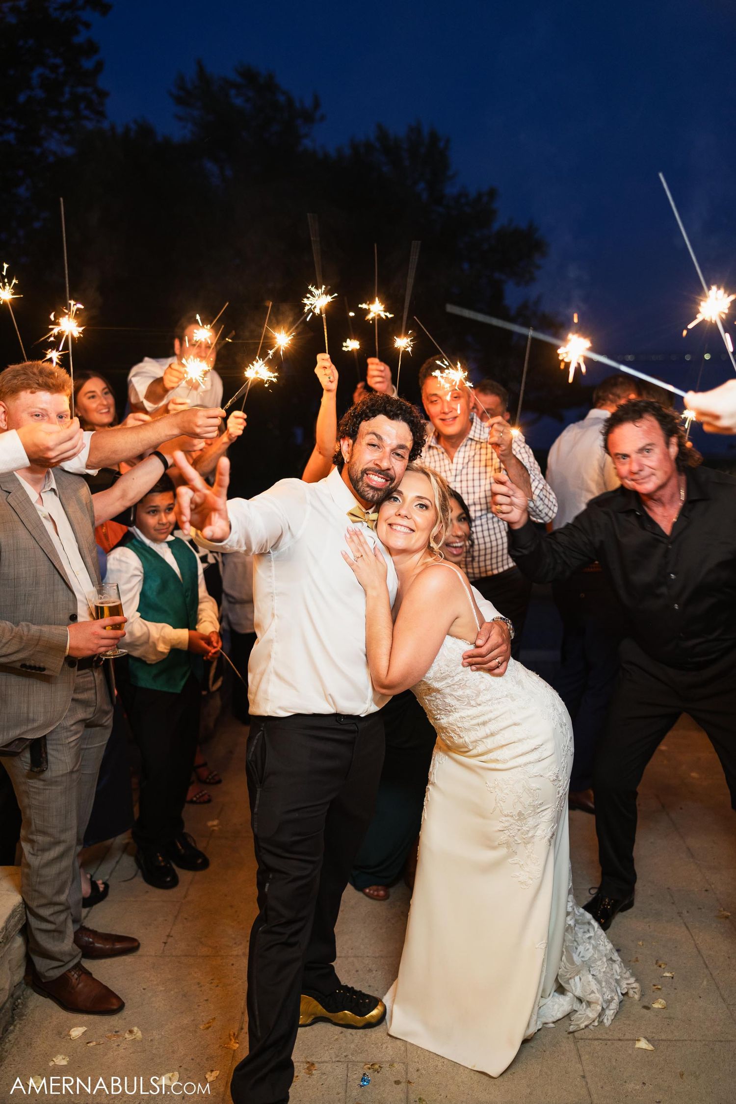 Wedding party celebrates with sparklers at nighttime outdoor reception.