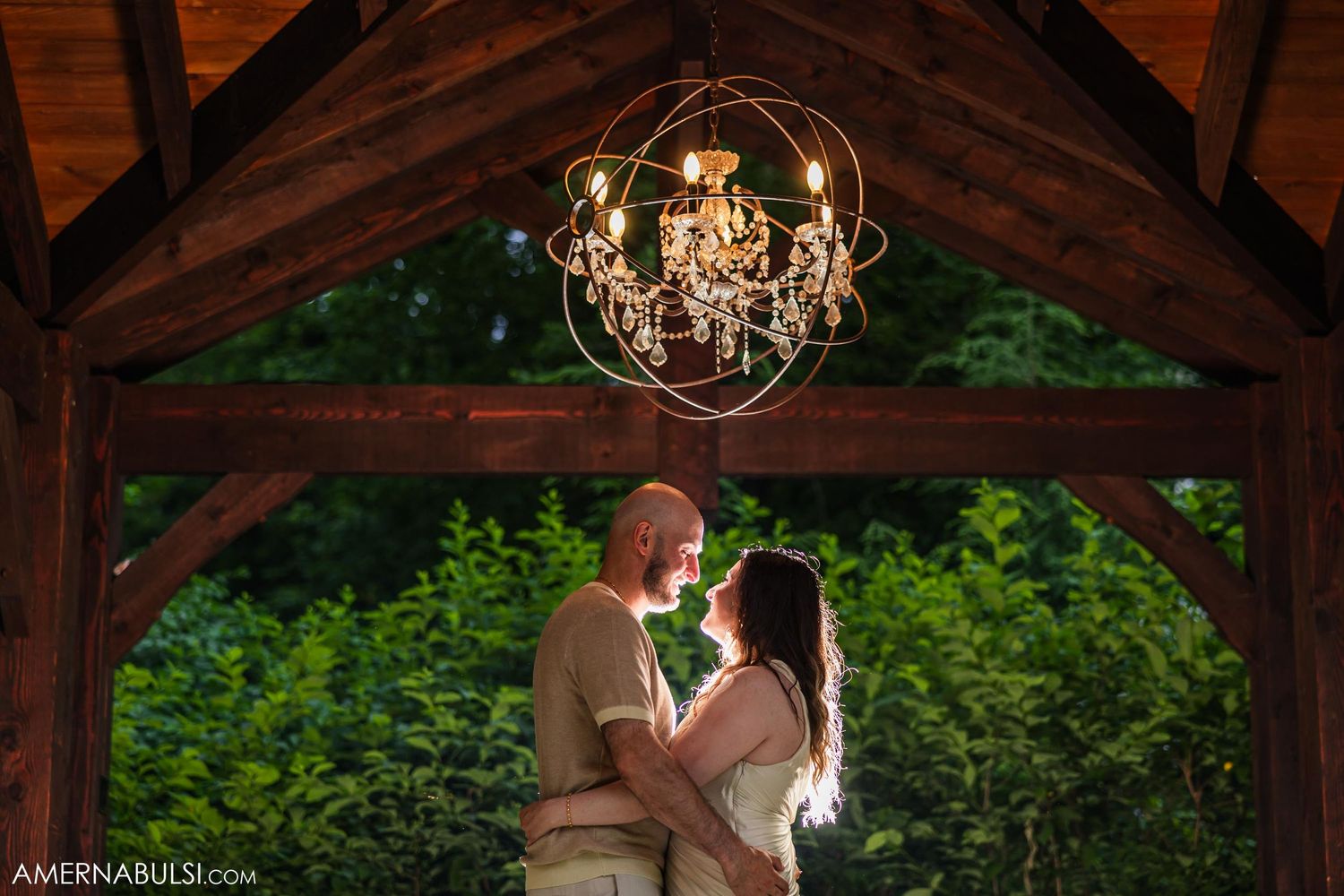 A romantic moment under a crystal chandelier in a rustic wooden gazebo during a wedding celebration.