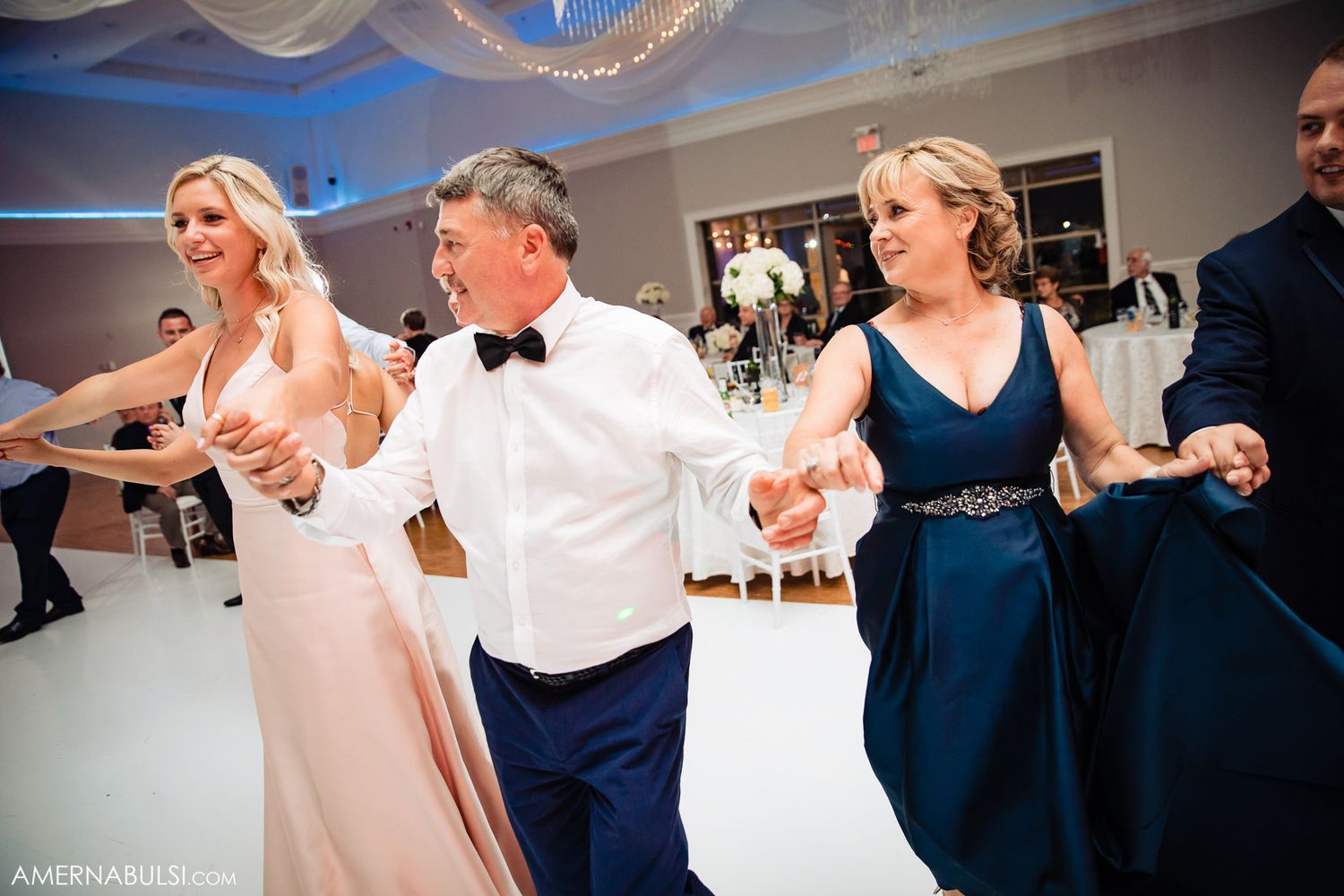 Wedding guests dancing in a line on a white dance floor under blue lighting.