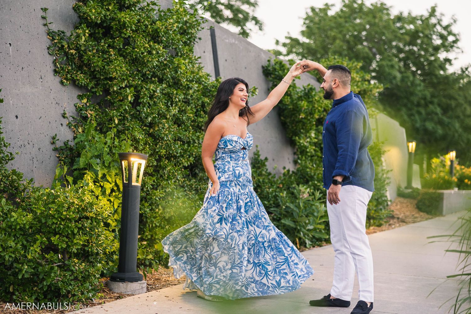 Dancing couple in blue floral dress and navy outfit on an outdoor garden pathway.