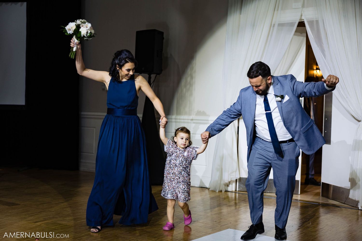 Dancing celebration at wedding reception with attendants in navy and grey alongside young guest.