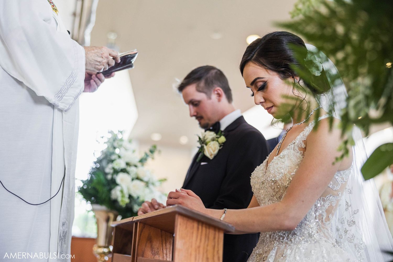 A wedding ceremony in progress with a priest officiating as the couple participates in traditional rituals.