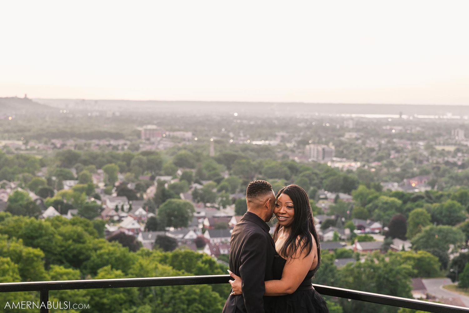 A romantic moment captured at sunset overlooking a scenic city view from an elevated vantage point.