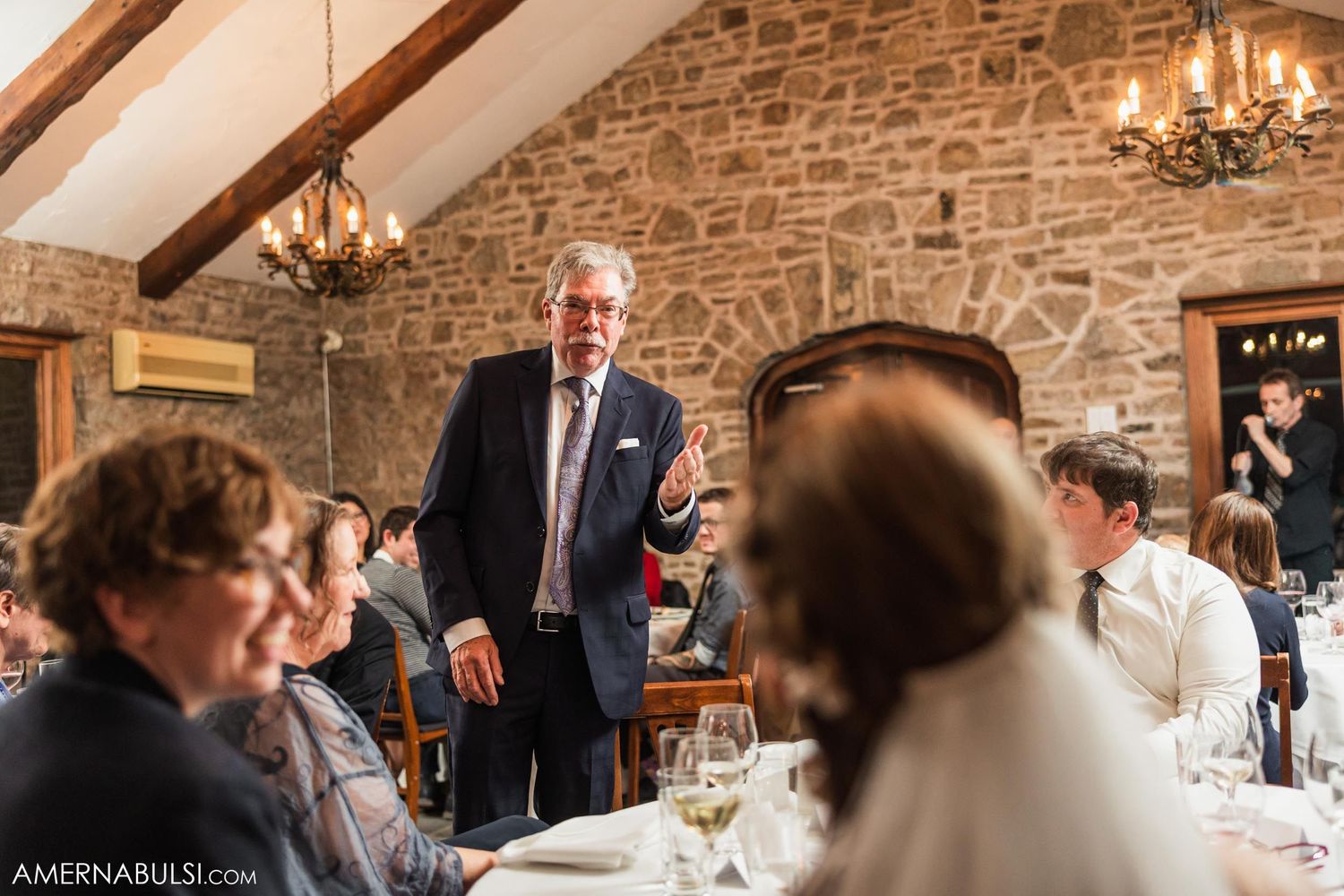 A guest stands to give a speech during the wedding reception in a rustic stone venue.