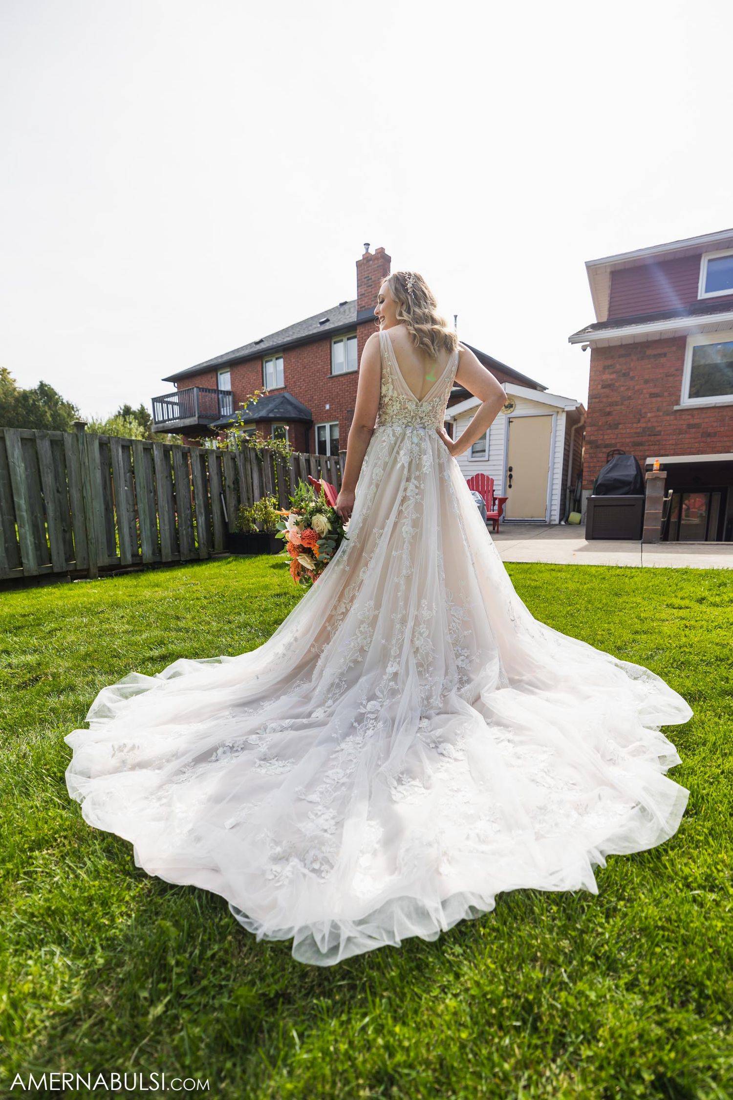 A stunning lace wedding gown with cathedral train displayed on green lawn behind brick house.