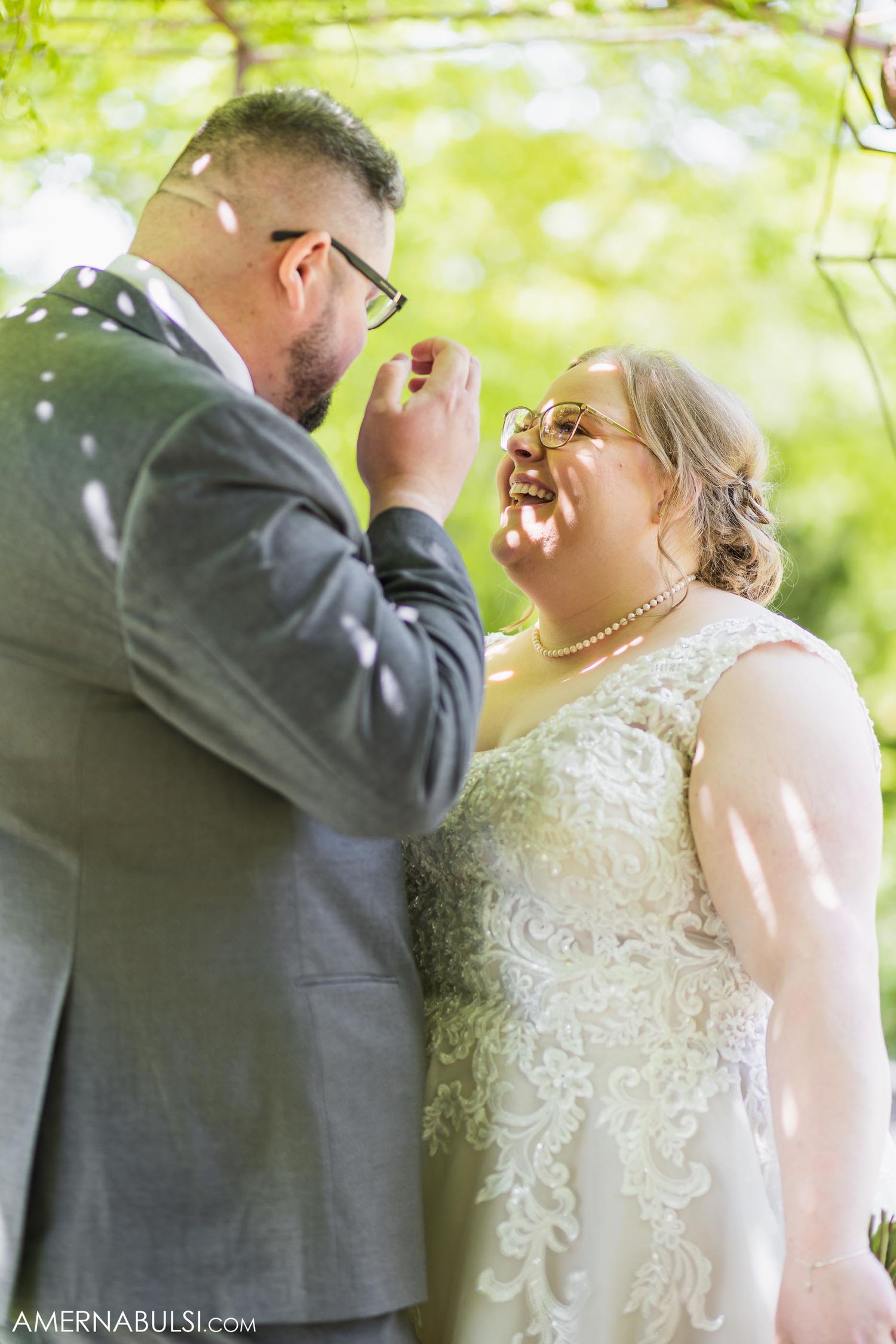 Joyful wedding couple sharing an emotional moment under green foliage.