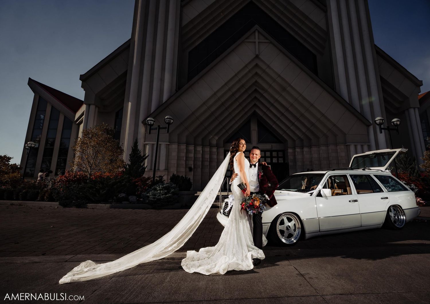 Dramatic architectural wedding portrait with white vintage station wagon outside modern church.
