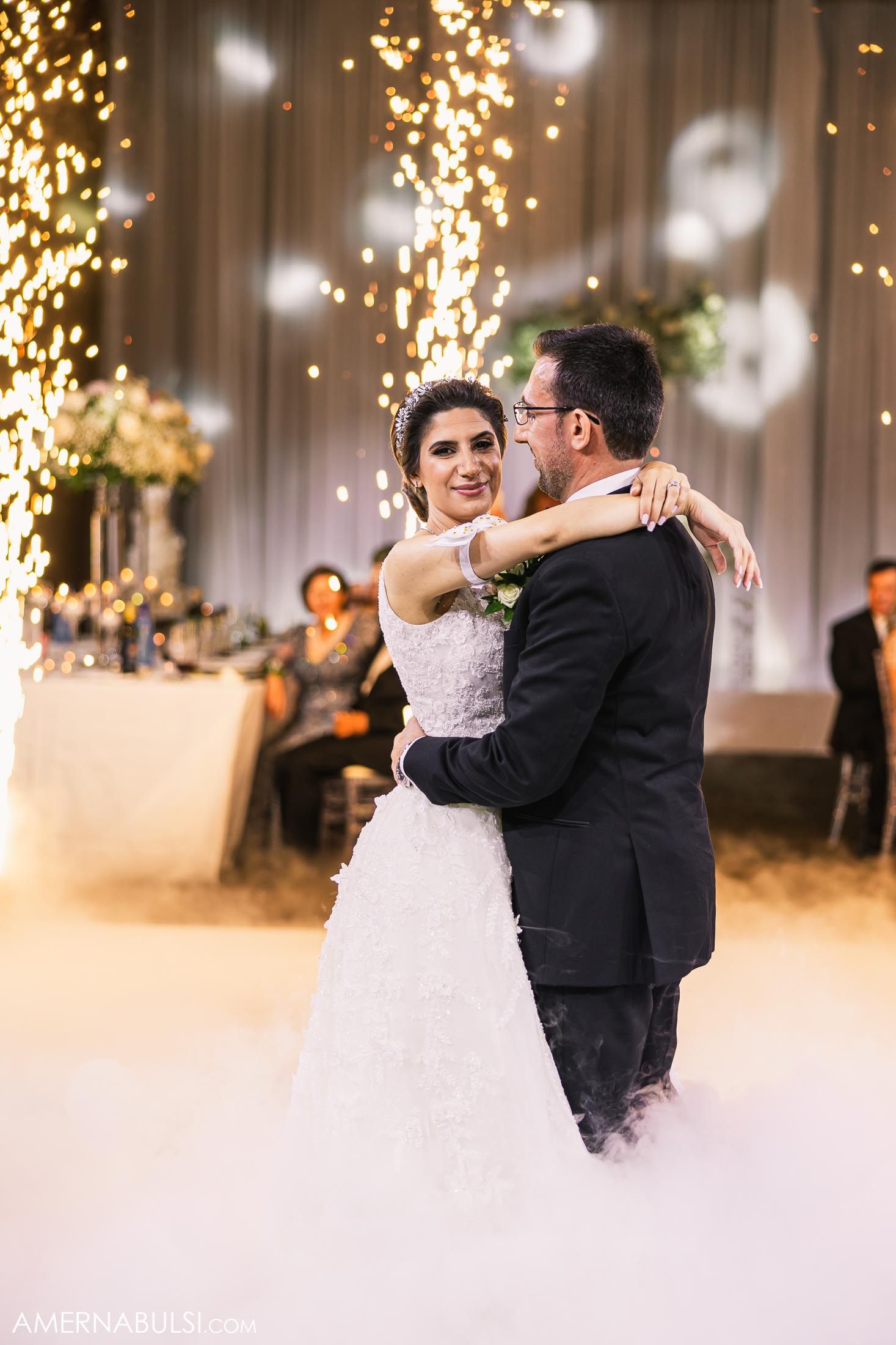 Newlyweds share an intimate dance moment surrounded by sparkling fountains and fog effects.