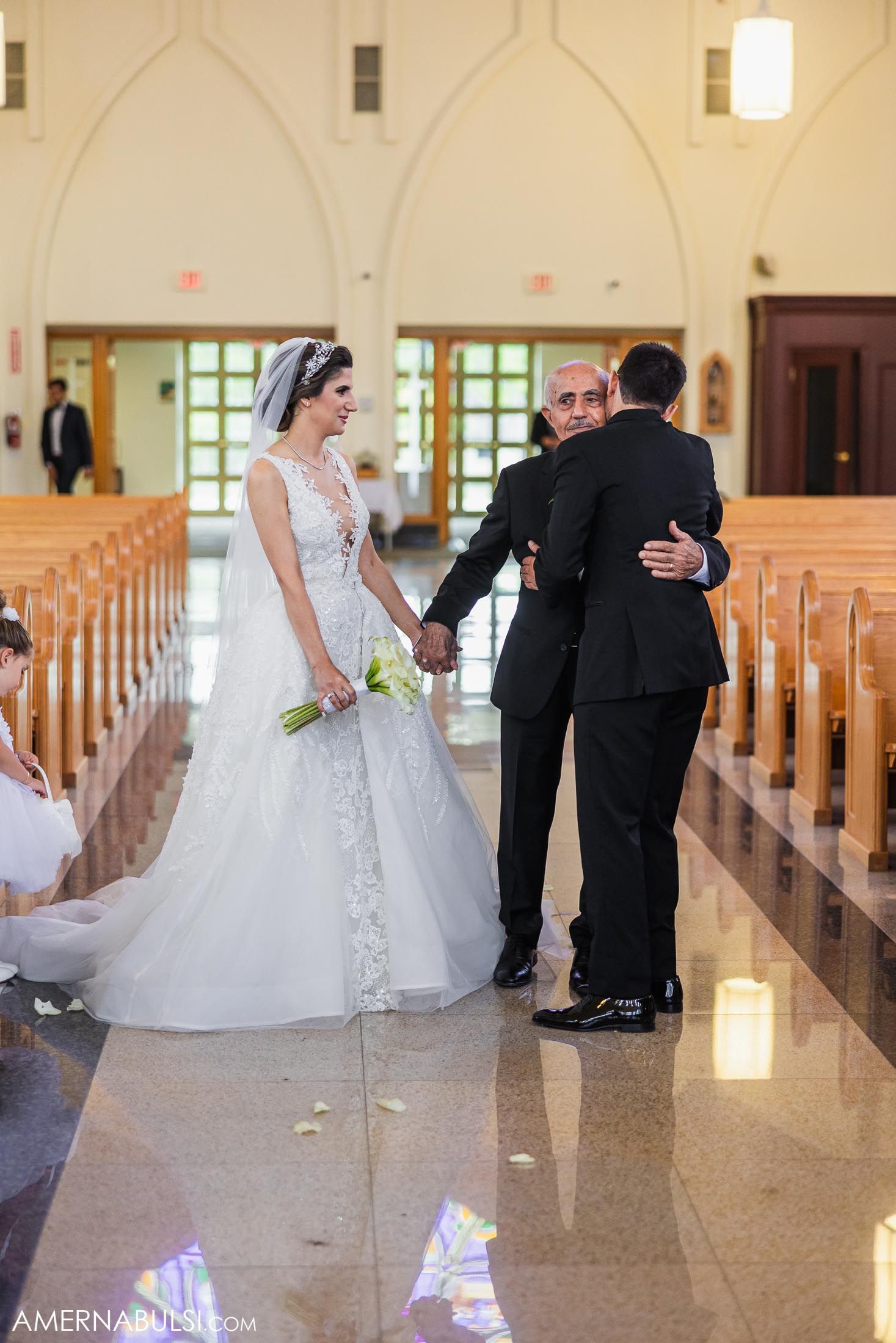 A wedding party gathers in a church aisle with Gothic arched windows and wooden pews.